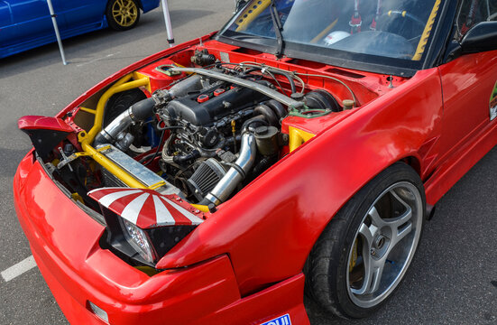 Red Nissan 200SX S13 with its hood open, showcasing a modified engine bay highlighting the car's custom modifications and performance focus