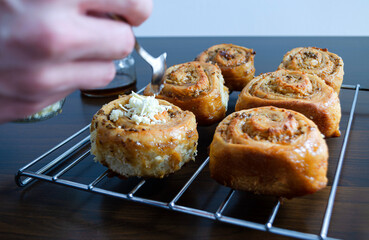 Mano con cuchara vertiendo queso sobre golfeado o rollo de pan dulce recién horneado. 