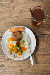 A plate of food and a glass of tea on a wooden table. Rice and vegetable soup with fried tempeh and tofu