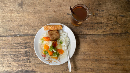 A plate of food and a glass of tea on a wooden table. Rice and vegetable soup with fried tempeh and tofu