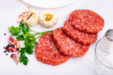 Raw ground beef meat steak burgers cutlets on white plate close to garlic, pepper and parsley in a restaurant