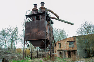 Rusty structure towers over wild grass and trees in an abandoned industrial site, showcasing a forgotten era of manufacturing and decay