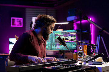 Sound engineer working in home studio with daw software interface, playing piano notes and editing audio recordings. Performer creating tunes on electronic midi controller keyboard.