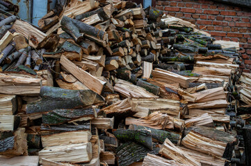 Stacks of firewood arranged neatly against a brick wall, ready for use during cold weather. The wood shows signs of being freshly cut