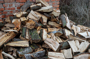 Firewood is neatly piled next to a rustic brick wall, surrounded by sparse vegetation in a serene outdoor setting at dawn