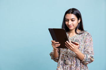 Indian person excited to purchase stuff adding payment method on website with her tablet, isolated over studio background. Ecstatic client does internet shopping, typing debit card info.