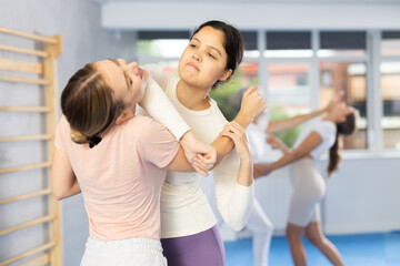 With full concentration, young Asian woman in self-defense workout grasping female opponent arm and...
