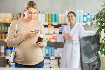 Obraz premium Pregnant woman in pharmacy scans QR code on medicine syrup product, checks certificate on manufacturers website. Girl pharmacist offer similar product in background.