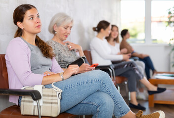 Fototapeta premium Bored skilled mature lady executive manager with phone sitting in chair waiting meeting recruiter. concept of vertical labor migration, mobility