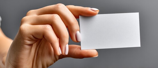 Obraz premium A clean, close-up image of a hand holding a blank white business card against a neutral background.