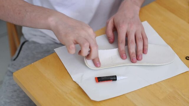 A young man repairs the insole of a sneaker at home.