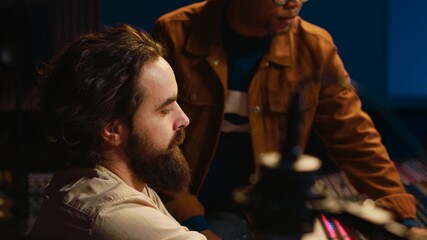 Musician and producer work on soundboard pads at professional studio station. Sound designer uses digital mixer in music production, operating on sliders and key buttons at control desk. Camera A.