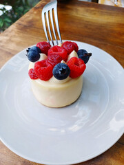 Pastel de crema y frutos del bosque con un tenedor sobre una mesa de madera. Plano Vertical.