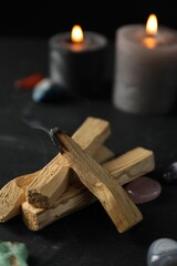 Smoldering palo santo stick, gemstones and burning candles on black table, closeup