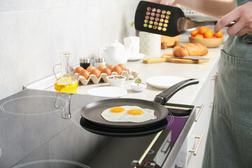 Woman with slotted turner cooking eggs in frying pan on cooktop indoors, closeup