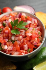 Delicious salsa in bowl and ingredients on grey table, closeup