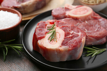 Pieces of raw beef, rosemary and salt on wooden table, closeup
