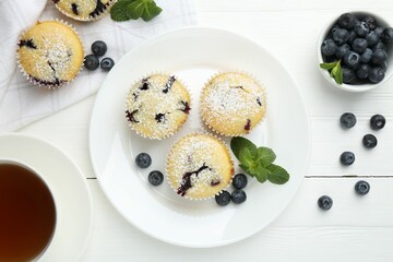Delicious muffins with blueberries, powdered sugar and mint on white wooden table, flat lay