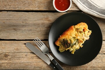 Tasty vegetable casserole, sauce and cutlery on wooden table, flat lay. Space for text