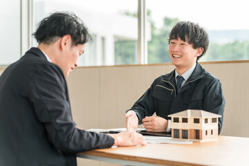 住宅模型や設計図を使って顧客にマイホームの説明・商談をするビジネスマン
