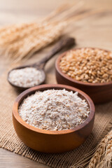 Whole wheat flour with wheat grain in bowl on wooden background