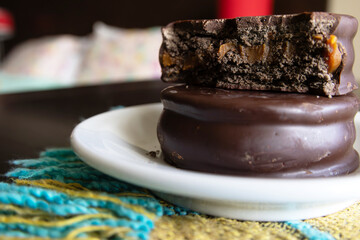 Two dark chocolate alfajores photographed up close, one is half full showing the dulce de leche filling on top of a whole alfajore