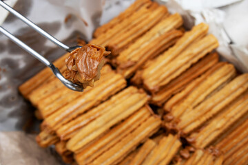 A churro filled with dulce de leche being held with tongs and a portion of churros inside a basket in the background out of focus