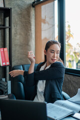 Professional woman in a modern office environment, taking a break and stretching by a large window with natural light.