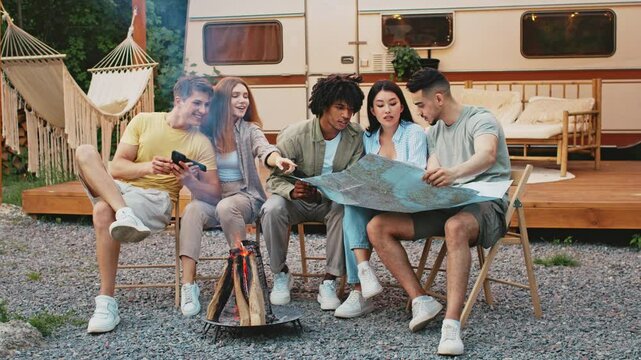 A diverse group of friends enjoys a relaxing summer day outdoors, gathered around a campfire while discussing their weekend camping plans. Checking the map - Powered by Adobe