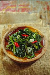 Cah kangkung or tumis kangkung or Vegetable kale, food from Indonesia, on a wood plate