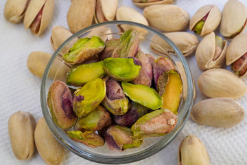 Salted pistachios in a glass bowl and scattered around on a white background, isolated, side view, crunchy roasted nuts,tasty,nutritious snack, healthy organic food, high-protein.