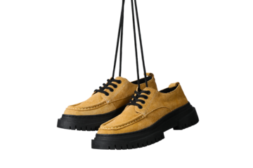 Brown shoes with black soles hang by their laces, showcasing design, isolated on white