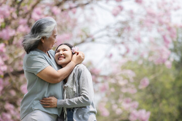 Fototapeta premium A joyful moment between an elderly woman and a young woman as they laugh together beneath blooming pink trees. Their warm embrace and shared laughter reflect the deep love of family and nature.