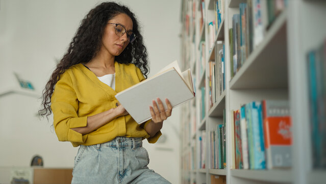 Latina Caucasian Hispanic woman learning teacher girl student female studying college browsing bookcase searching book read bookshelf looking literature library search textbook take find university