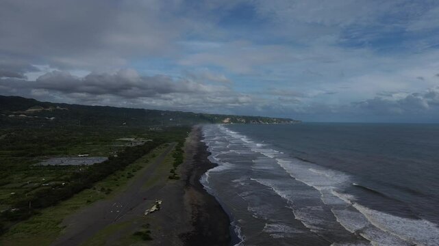 Scenic coastal landscape with waves gently rolling to the black sandy beach under dramatic sky on Depok Beach Yogyakarta