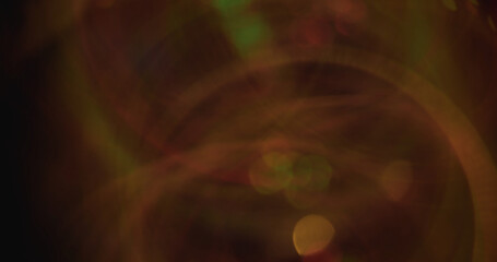 Blur flare swirling. Defocused sparkling mystery. Orange green multicolor blaze lens glow motion on dark black blurred bokeh light background.