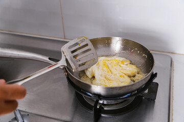 Man cooking fried egg in a frying pan on the stove. 
