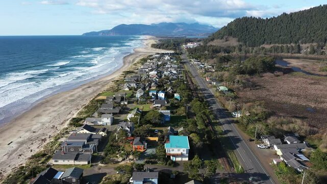 4K aerial drone video of Rockaway Beach on the Oregon Coast, showing waves of the Pacific Ocean, small coastal town, sunset, sandy shoreline, forested mountains. Perfect for travel and tourism themes