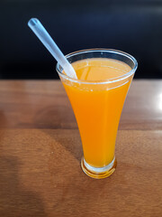 Hot Orange Drink in a Glass with Straw on Wooden Table