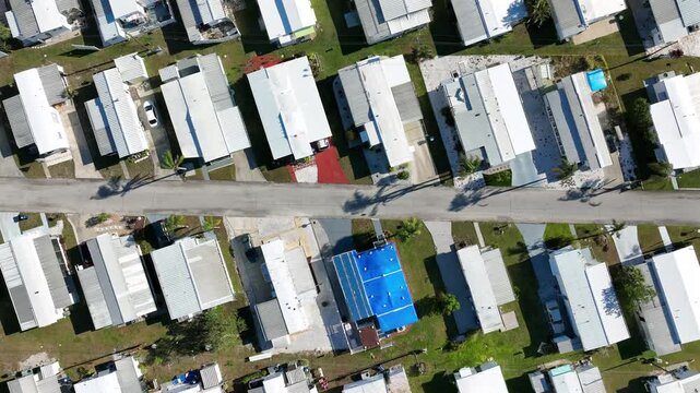 Aerial top down of american small and tiny houses in trailer home park of Florida. Sunny day with palms on street. Descending shot. Roofs of homes.