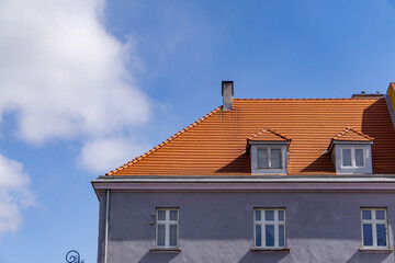 facade of a classic building with a red, sloping roof and white windows, under a blue sky with delicate clouds. An architectural style typical of European buildings from the beginning of the 20th cent