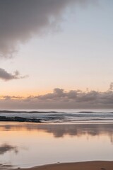 Obraz premium Serene coastal landscape at dawn with tranquil ocean waves reflecting soft pastel sky and wet sand beach creating peaceful atmosphere