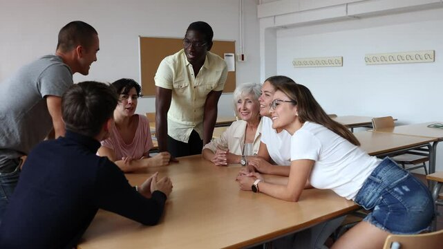 Diverse people sitting at desk during language courses in classroom. Senior and young people listening to native speaker teacher.