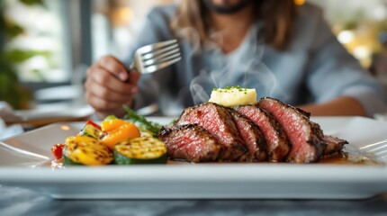 Steak with vegetables elegantly plated, sliced flank steak fanned on white ceramic dish with melting herb butter, alongside grilled zucchini, red peppers and yellow squash