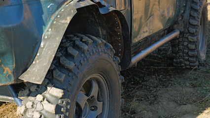 Close-up of a muddy off-road tire with a deep tread pattern. The tire is mounted on a vehicle with...