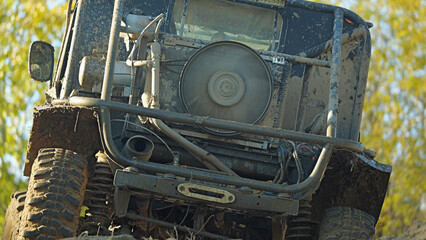 A muddy off-road vehicle traversing difficult terrain. The radiator and cooling fan of the vehicle can be seen. The SUV is covered with dirt and dust. Rear view.