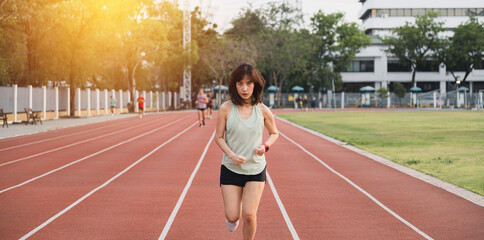 Fototapeta premium focused southeast Asian woman runner is jogging on red track in outdoor stadium during sunset, embracing healthy lifestyle and wellness with motivation and challenge