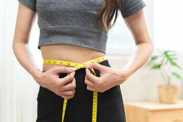 Weight lose, loss concept. Slim body asian young woman hand use tape measuring around waistline in...