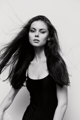 Elegant woman with long hair in a black dress, captured in motion against a minimalist white background. Fashion and beauty concept with strong expression.