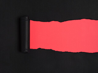 Ripped black rolled paper reveals a vibrant red underneath